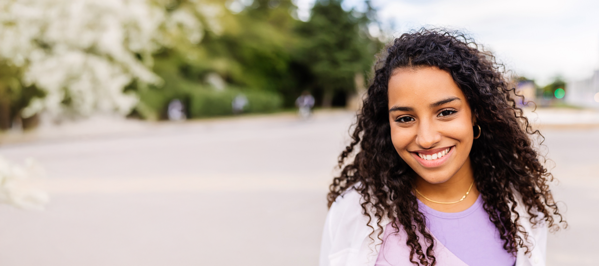 smiling young woman with dark curly hair wearing a purple shirt